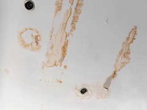 Brown water stains and peeling paint on a white ceiling around two recessed lights