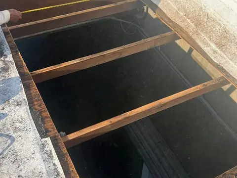 A section of flat roof opened down to the wood joists, with a tape measure held across the opening