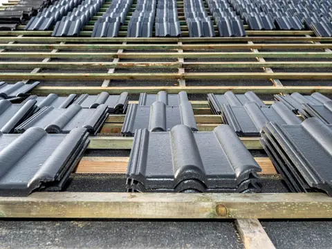 Dark grey roof tiles set out in small stacks on wood battens, with black underlayment showing between the battens